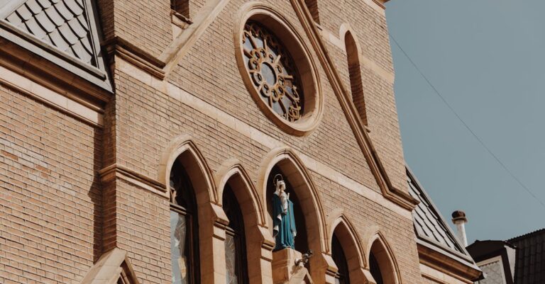 Close-up of a Gothic church facade featuring brickwork, stained glass windows, and religious statues.