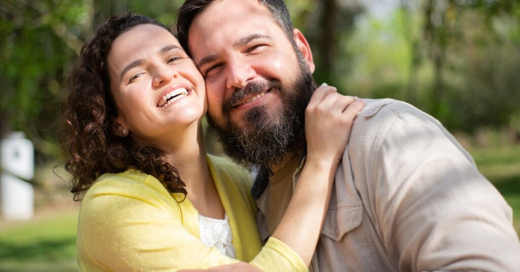 Happy couple smiling and embracing outdoors in a sunlit park, capturing a moment of joy and affection.