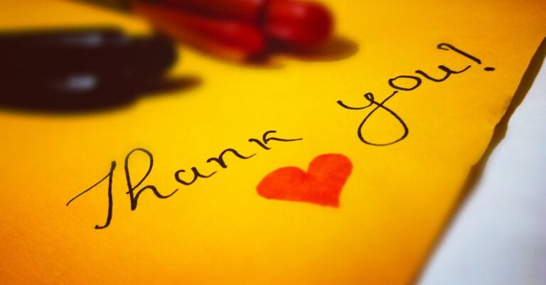 Close-up of a thank you note with a heart and pen on colored paper.