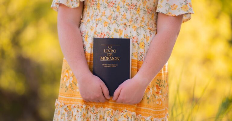 A child holds a Book of Mormon in a floral dress, set against a bright outdoor background.