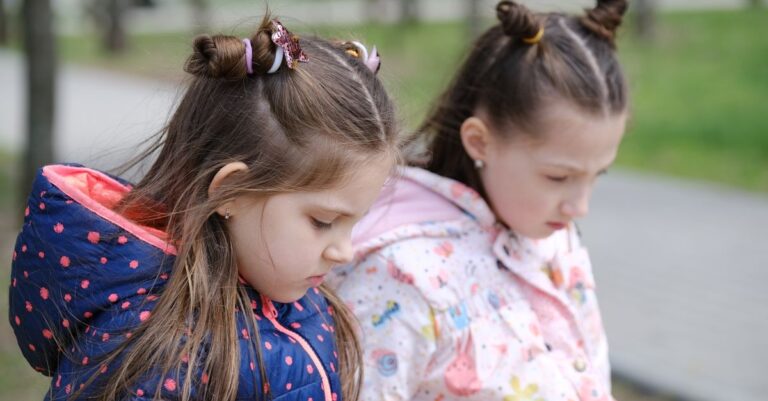 Two young girls in winter jackets, contemplative in a park setting.