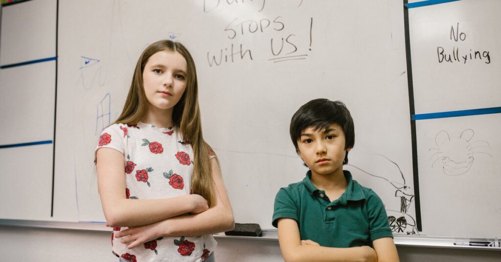 Two children standing confidently in front of anti-bullying message on classroom whiteboard.