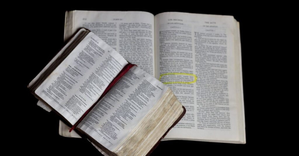 An open Bible on top of another against a plain black background.