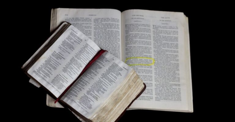 An open Bible on top of another against a plain black background.