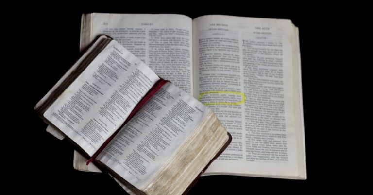 An open Bible on top of another against a plain black background.