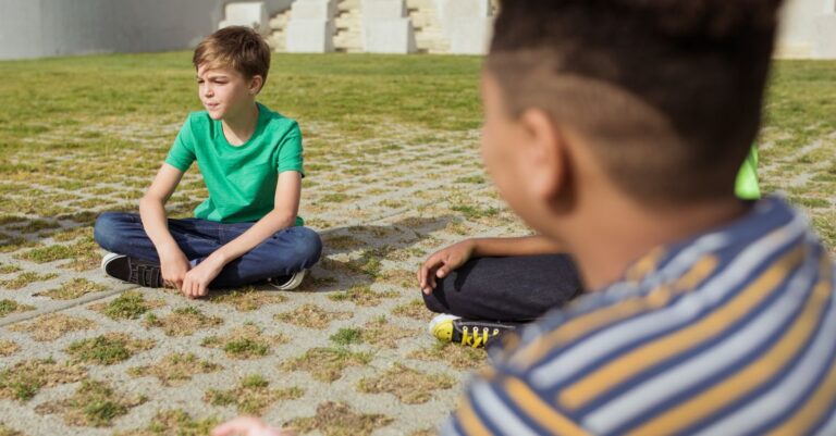 Group of children sitting in a park with bright sunlight, creating a peaceful atmosphere.