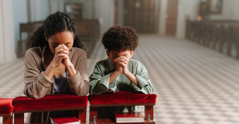 A mother and son kneeling and praying together inside a serene church.