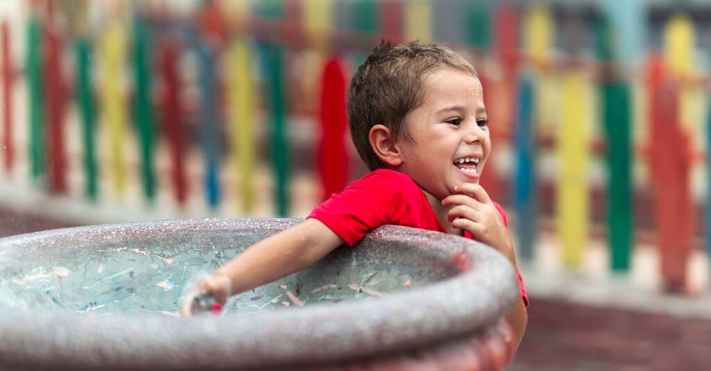 Happy child in a red shirt enjoying a playful moment at an outdoor water park.