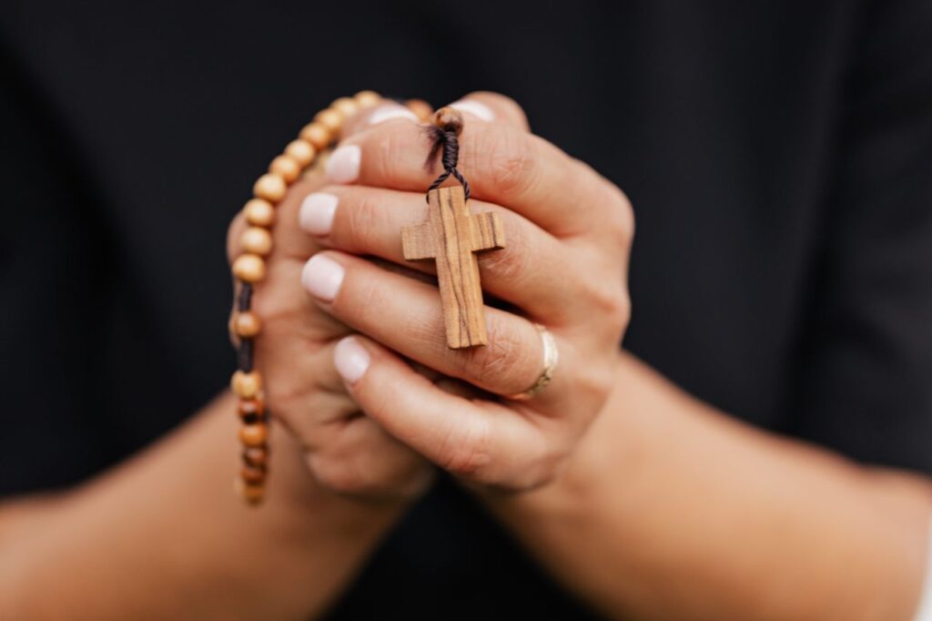 pexels-photo-5206837-5206837 A detailed close-up of hands clasping a wooden rosary with cross, symbolizing faith.