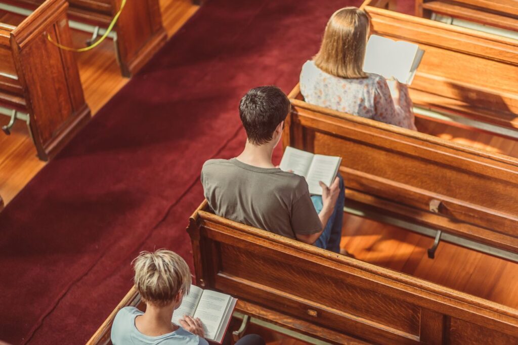pexels-photo-8674138-8674138 Three individuals reading books seated in a church pew, captured from above.