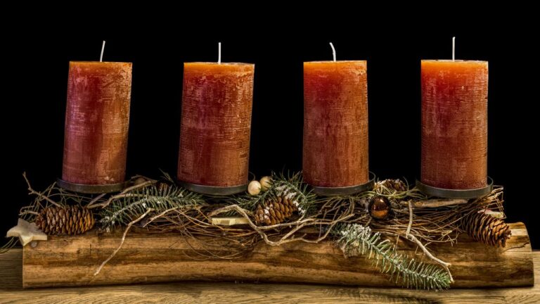 Four rustic advent candles on a wooden display with pine cones and greenery.