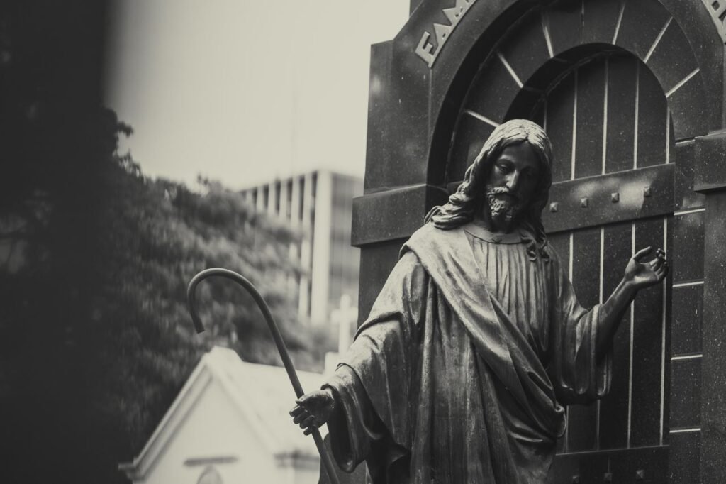 Black and white statue of Jesus Christ holding a cane in a cemetery setting.