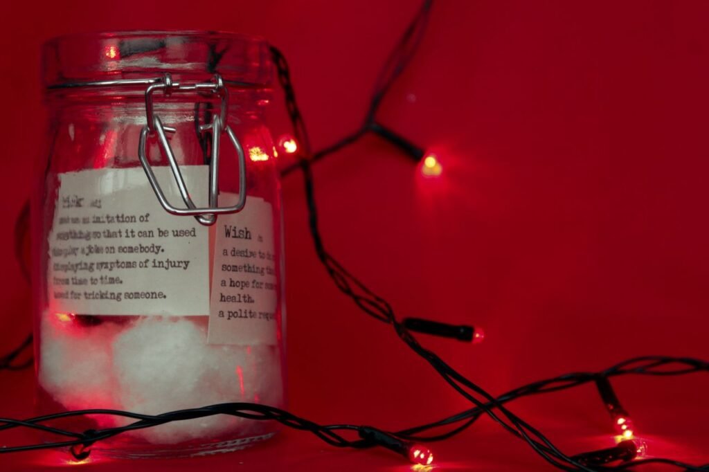 A festive glass jar with cotton and decorative lights on a red background, perfect for Christmas.