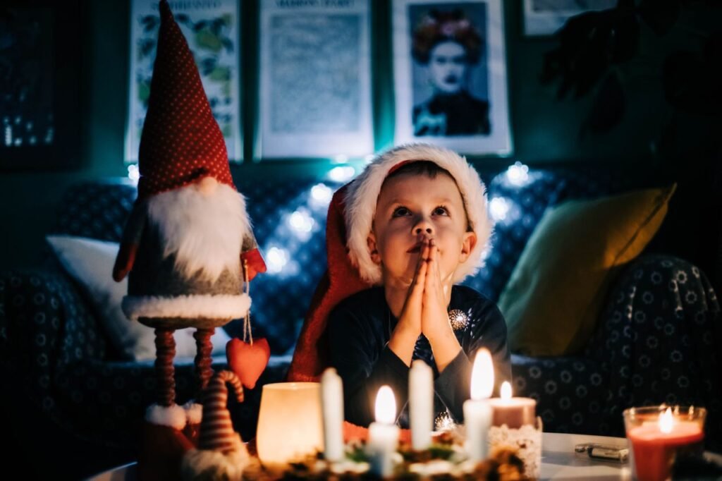 A child in a Santa hat makes a wish by candlelight in a cozy Christmas setting.