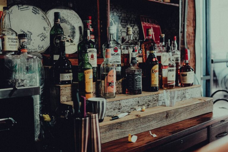 A collection of diverse liquor bottles including whisky, rum, and vodka displayed on a wooden bar shelf.