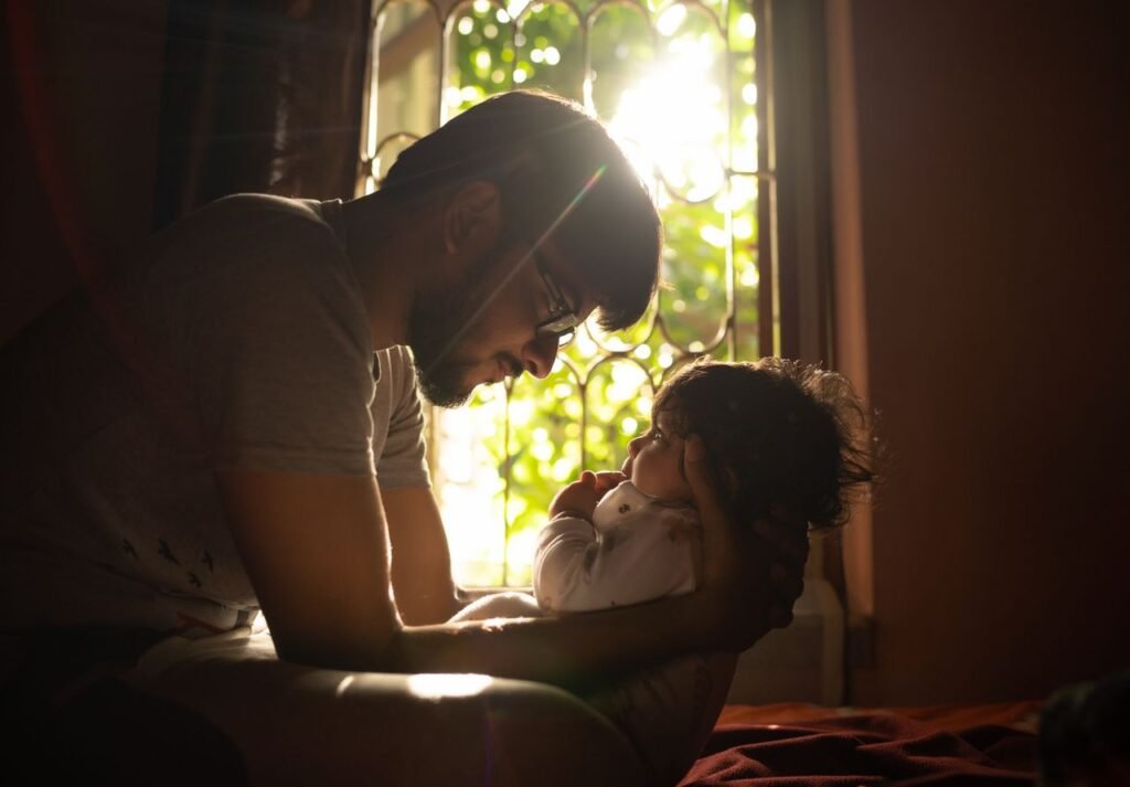 A touching moment between a father and child by a window with warm sunlight illuminating their bond.