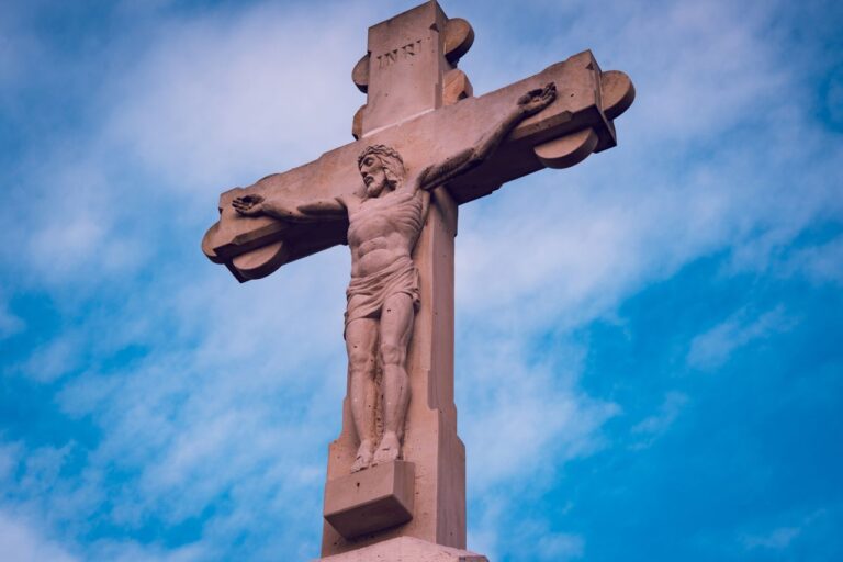 Statue of Jesus Christ on the cross under a vibrant blue sky, symbolizing Christianity.