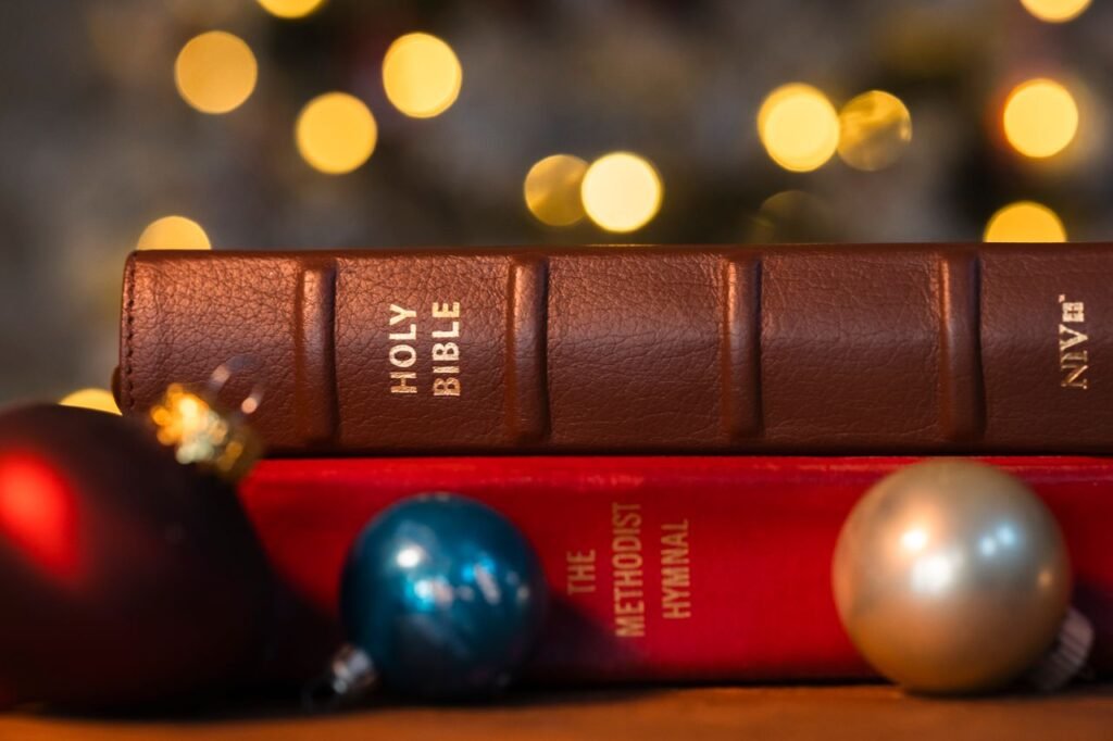 A Holy Bible and Methodist hymnal with Christmas ornaments and festive bokeh lights.