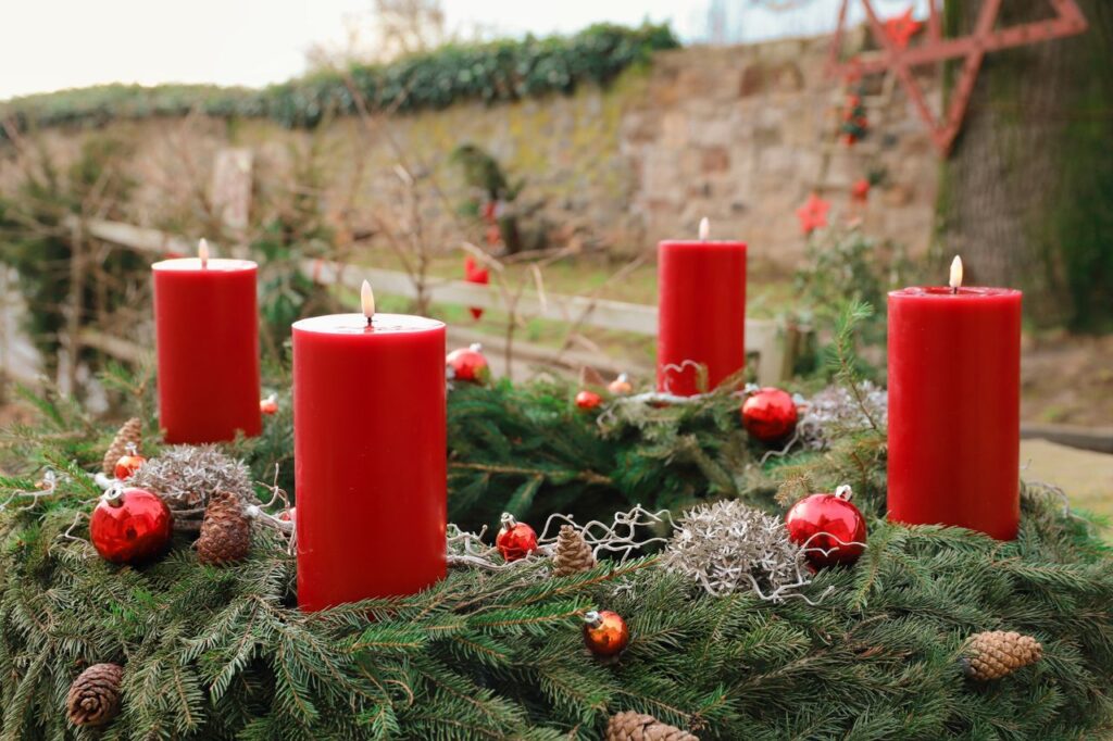 pexels-photo-29917906-29917906-1 A vibrant outdoor advent wreath with four red candles and pine decorations.