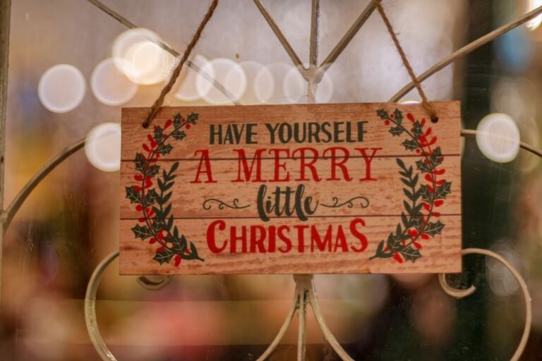 A wooden Christmas sign with festive message and bokeh lights background.