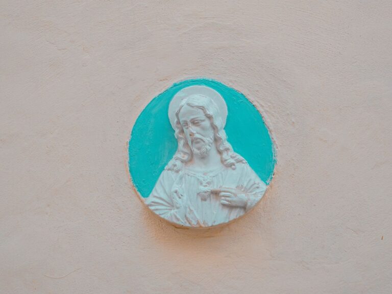A detailed limestone relief of Jesus set against a turquoise backdrop, reflecting religious art in Malta.