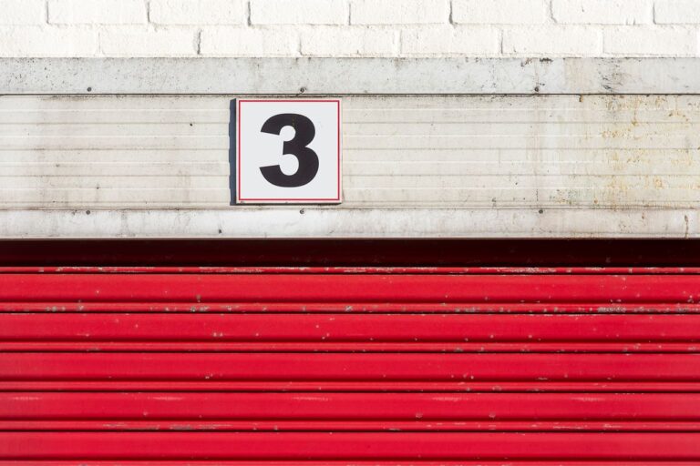 Close-up of a red garage door with a large number three sign above it.