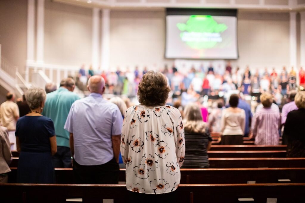A congregation stands in reverence in a church, facing a stage with a worship team and projection screen.
