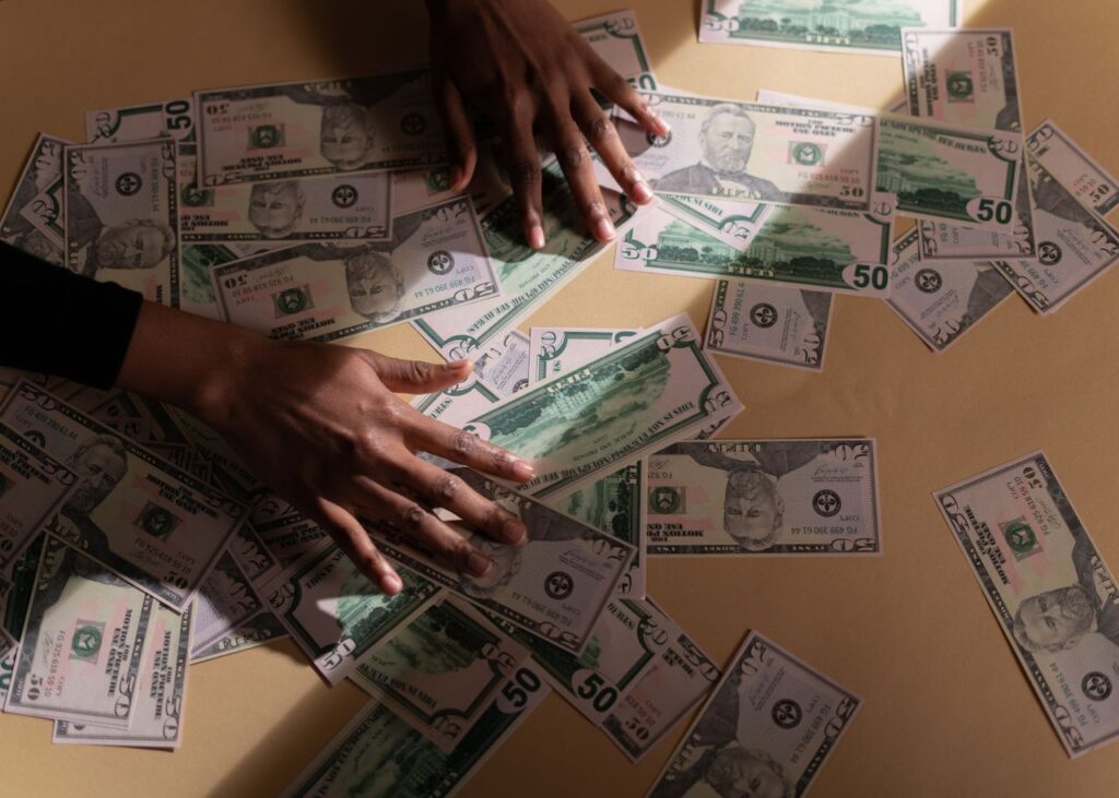 Hands arranging multiple US dollar bills on a table, depicting financial abundance and wealth.