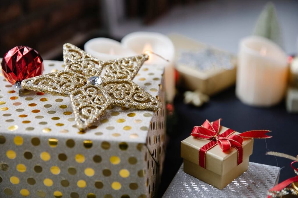 Various Christmas decorations with star on present boxes and red ribbon near balls and candles on black table in bright room
