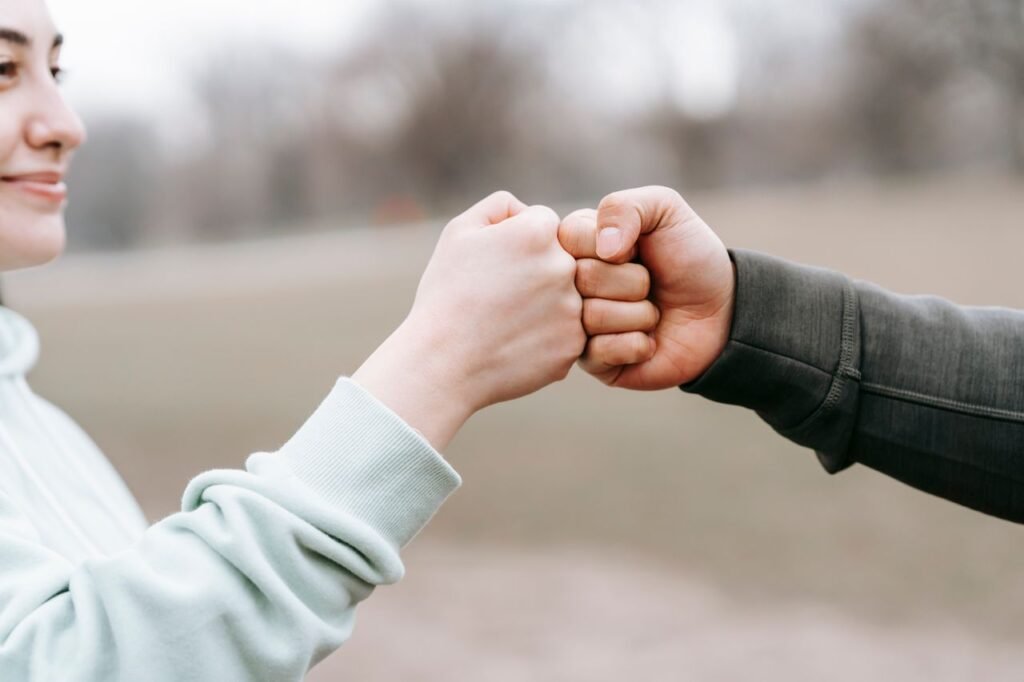pexels-photo-6551298-6551298 Crop anonymous cheerful woman and man giving fist bump to each other on blurred background of park