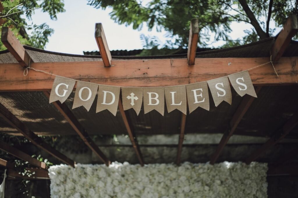 A charming pergola adorned with a 'God Bless' banner, set in a lush, outdoor environment.