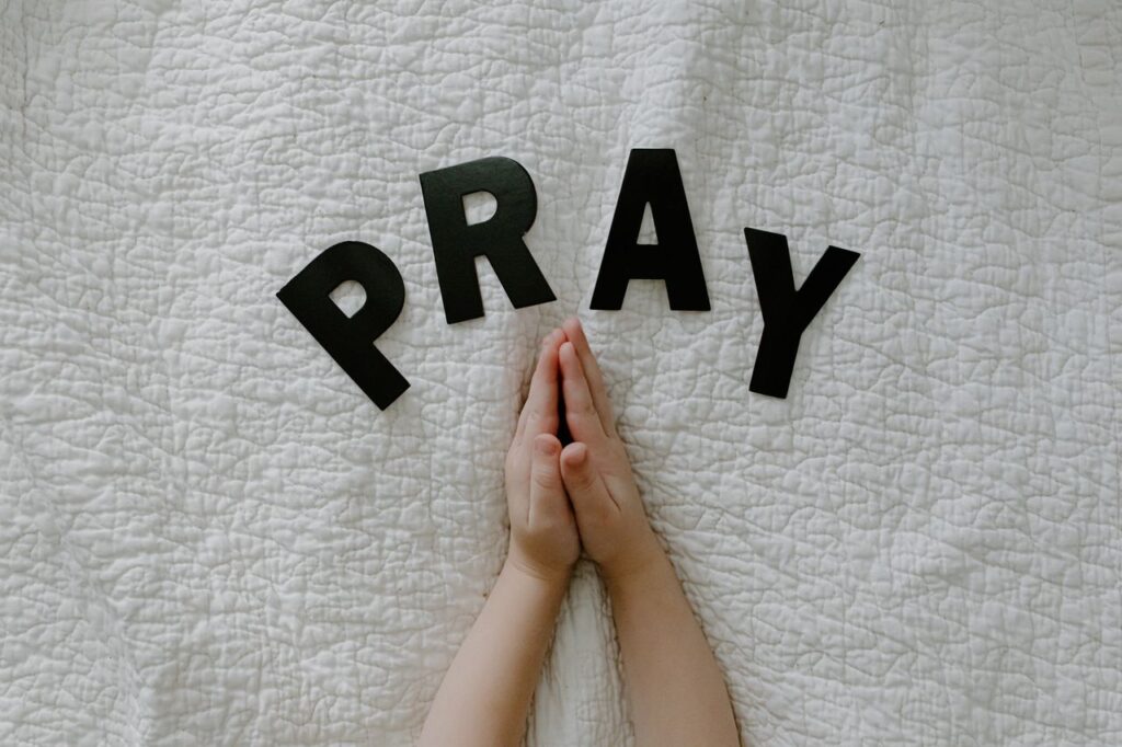 Close-up of hands in prayer on white quilted fabric with PRAY letters.