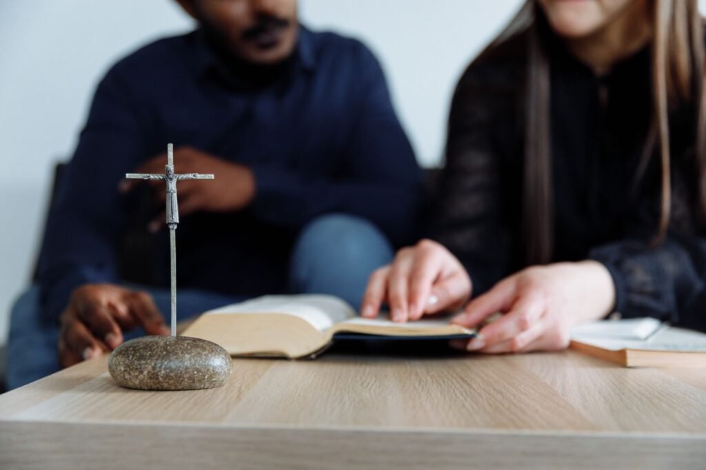 pexels-photo-8468742-8468742 Two individuals study the Bible with a cross on the table, symbolizing faith and devotion.