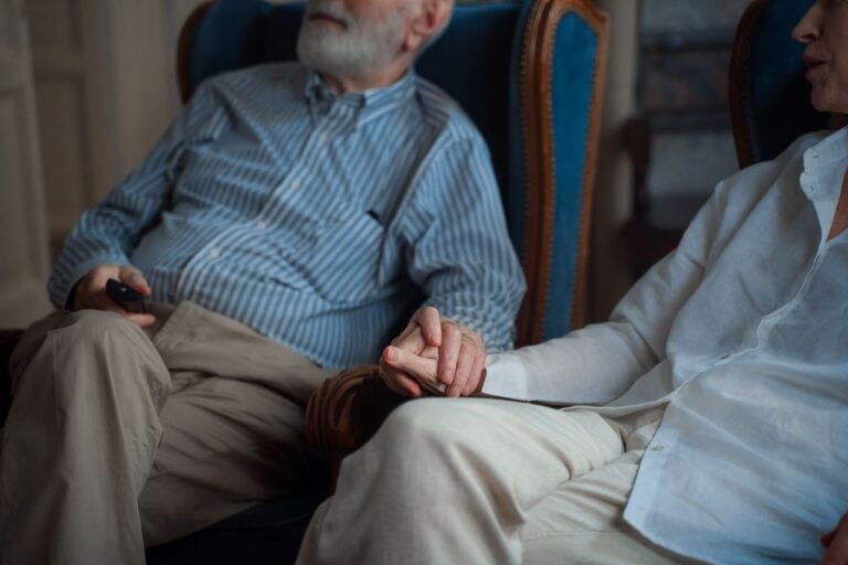 An elderly couple sitting together, holding hands in a cozy room, symbolizing companionship.